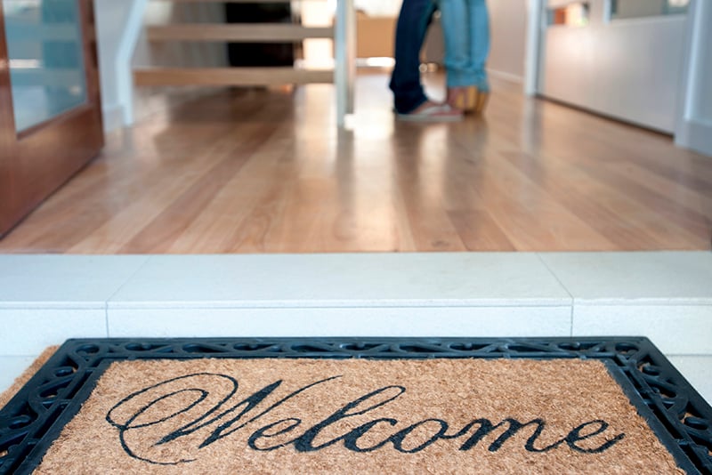 Welcome mat at entrance of home with people standing in doorway